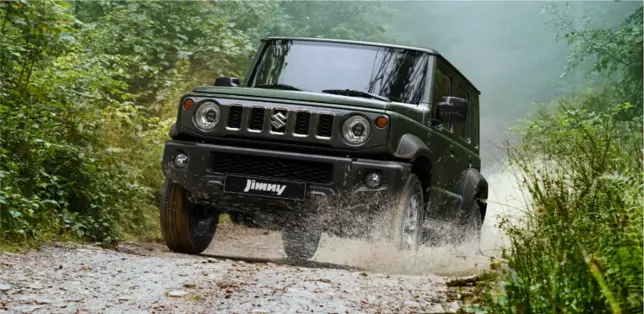 Suzuki Jimny 5 puertas, camioneta 4X4 en terreno enlodado con vegetación de fondo.